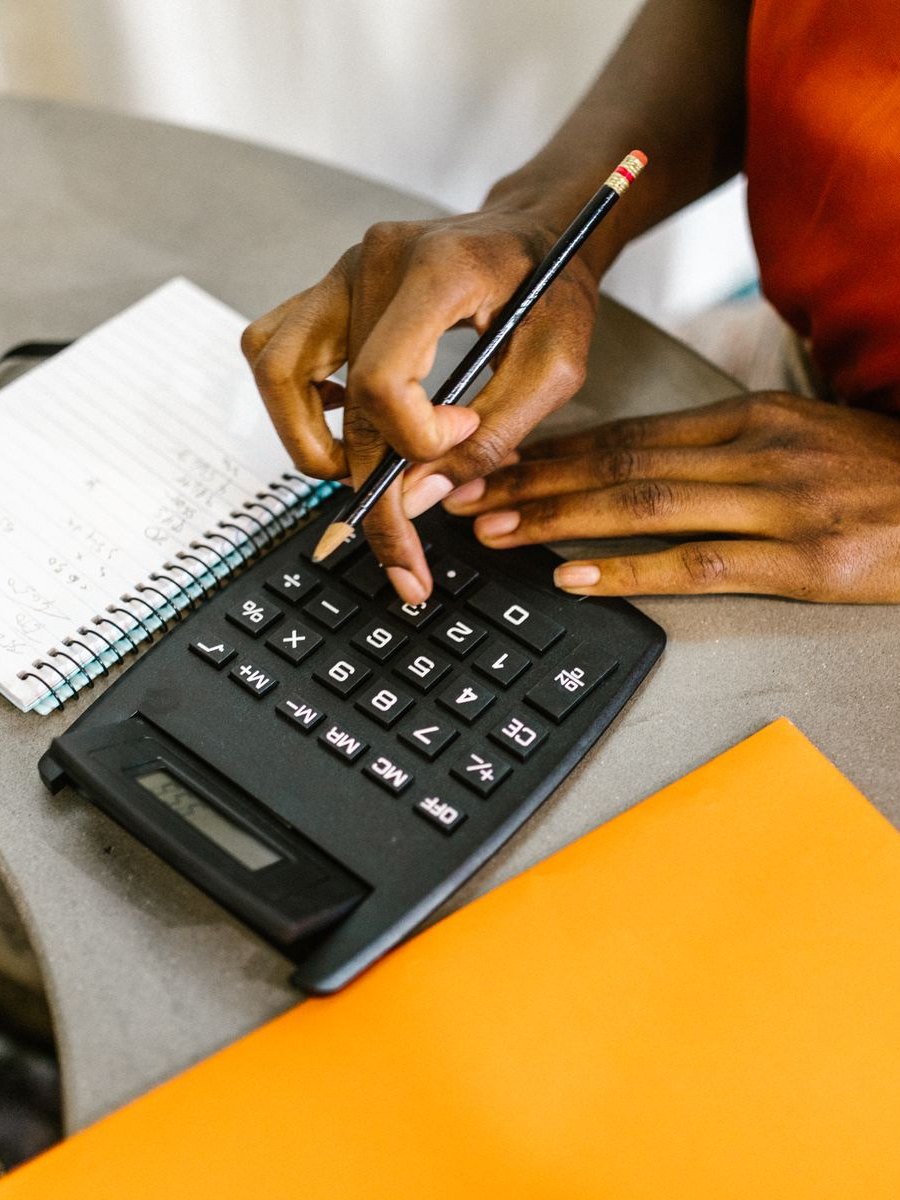 Mains sur une calculatrice à côté d'un carnet à spirale où des chiffres sont notés à la main