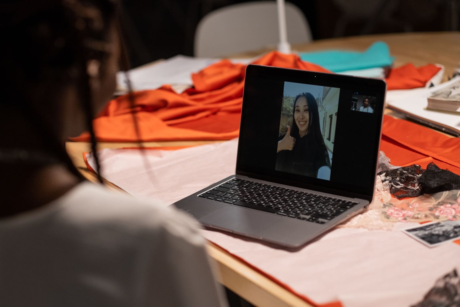 Créatrice de mode en visioconférence depuis son atelier, tissus orange sur la table, cliente souriante à l'écran