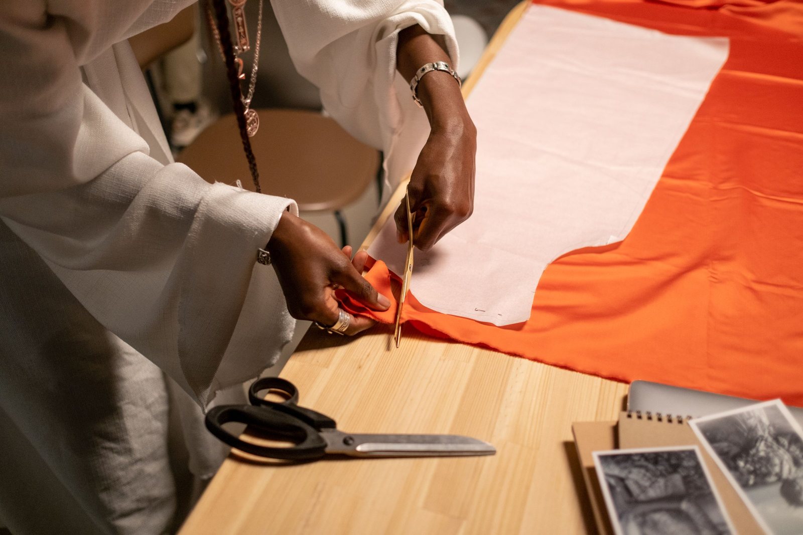 Mains d'une créatrice coupant du tissu orange sur un patron en papier, ciseaux posés sur la table