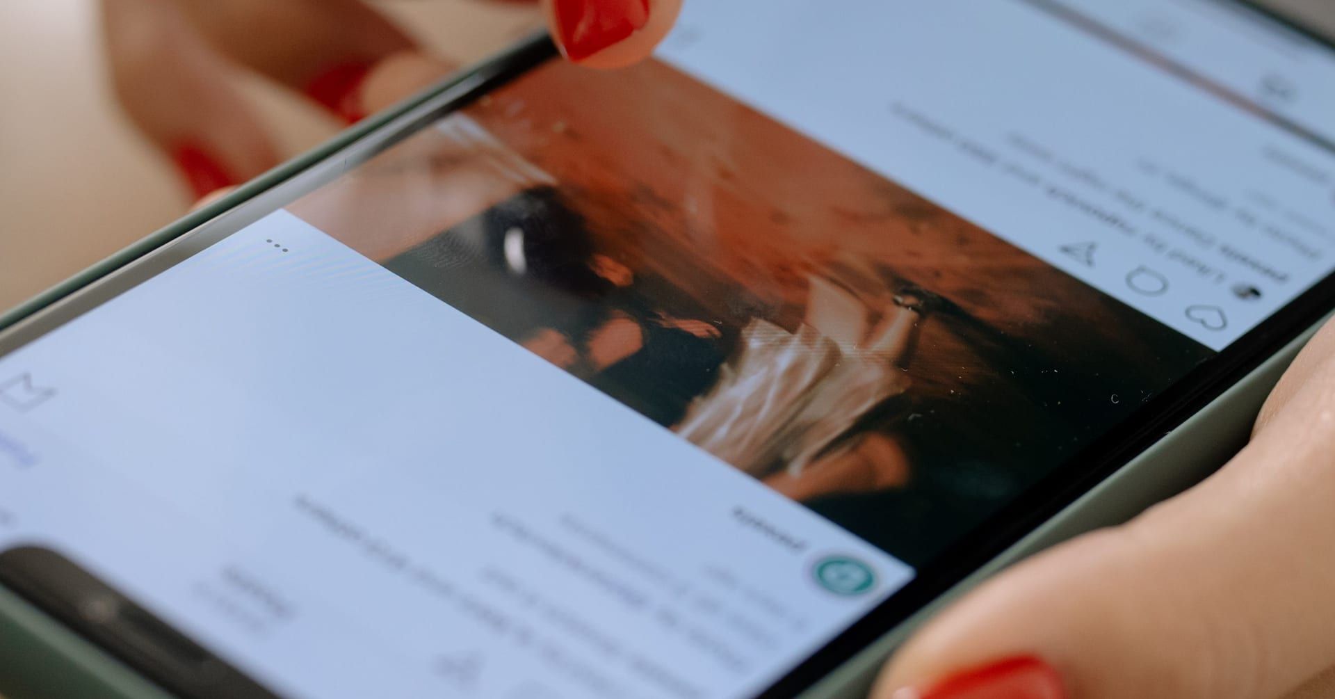 Main aux ongles rouges faisant défiler un post Instagram sur un smartphone