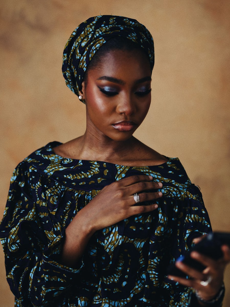 Femme en tenue wax et foulard assorti consultant son smartphone, pensive