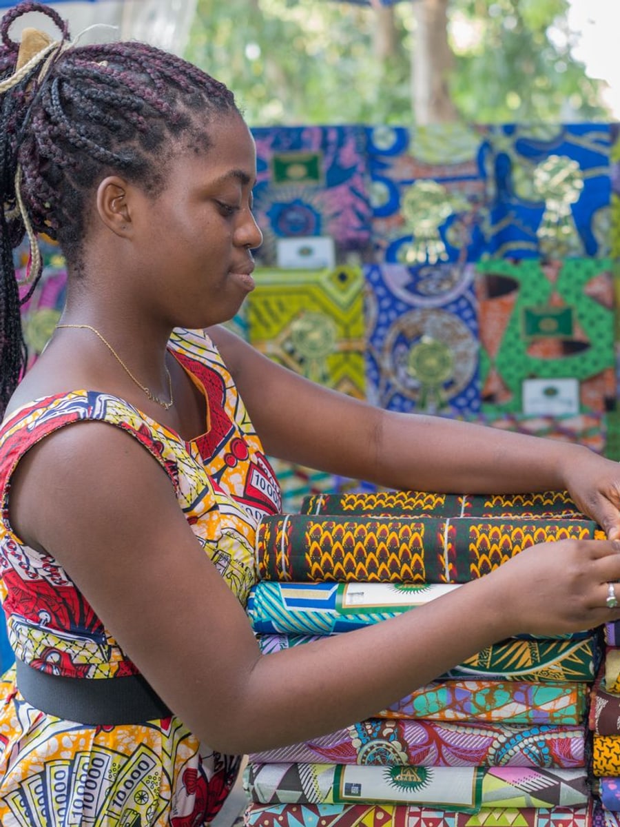 Jeune femme choisissant des tissus wax colorés sur un marché à Cotonou, au Bénin