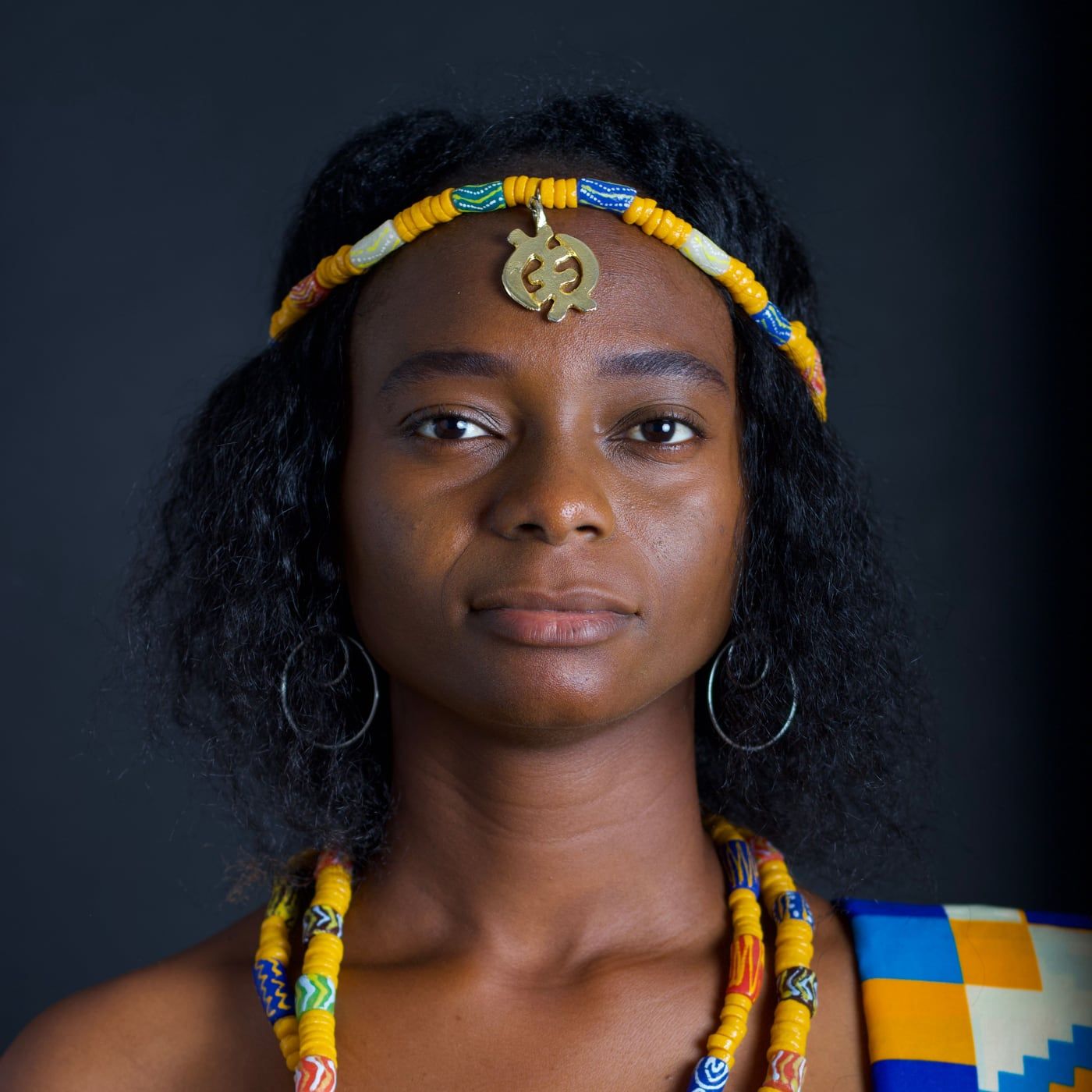 Portrait en studio d'une femme en habit traditionnel kente, bijoux et coiffe assortis